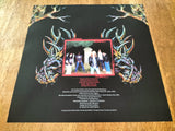 Black album cover with colorful designs and a photo of a band on a wooden surface